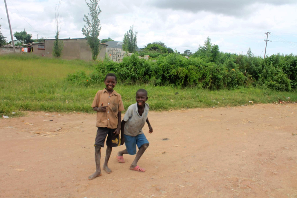 Two children smiling brightly into the camera while standing on a path